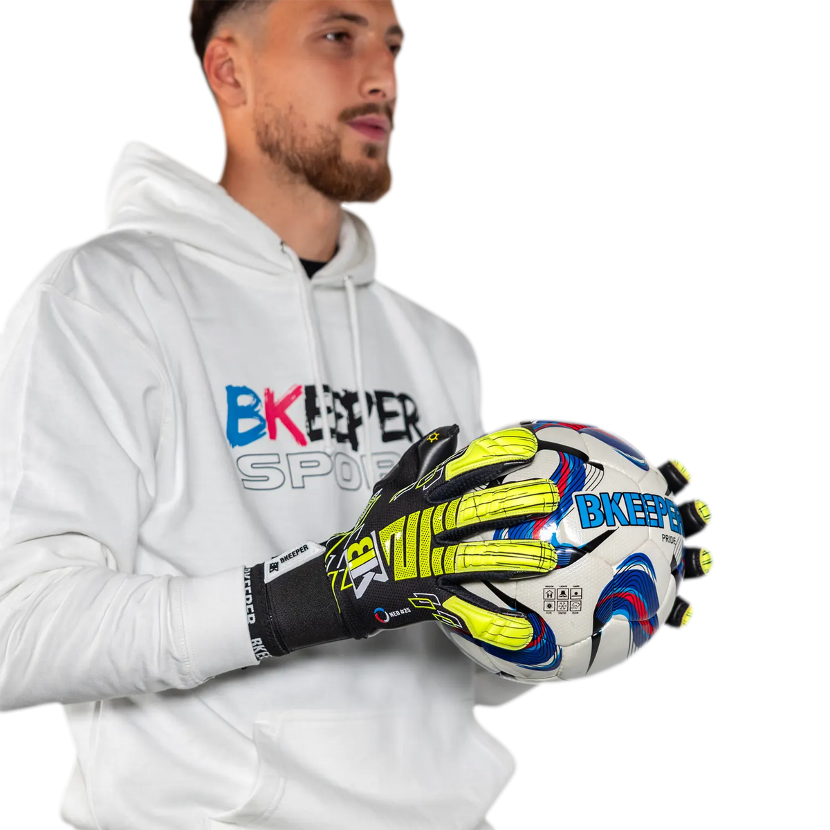 A man wearing a white BKeeper Sports hoodie holds a white goalkeeper glove with bright yellow, blue, and red accents. The background is solid white.